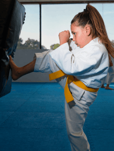 girl-kicking-bag-sm Girl kicking bag at Bernardo karate in a yellow belt karate gi
